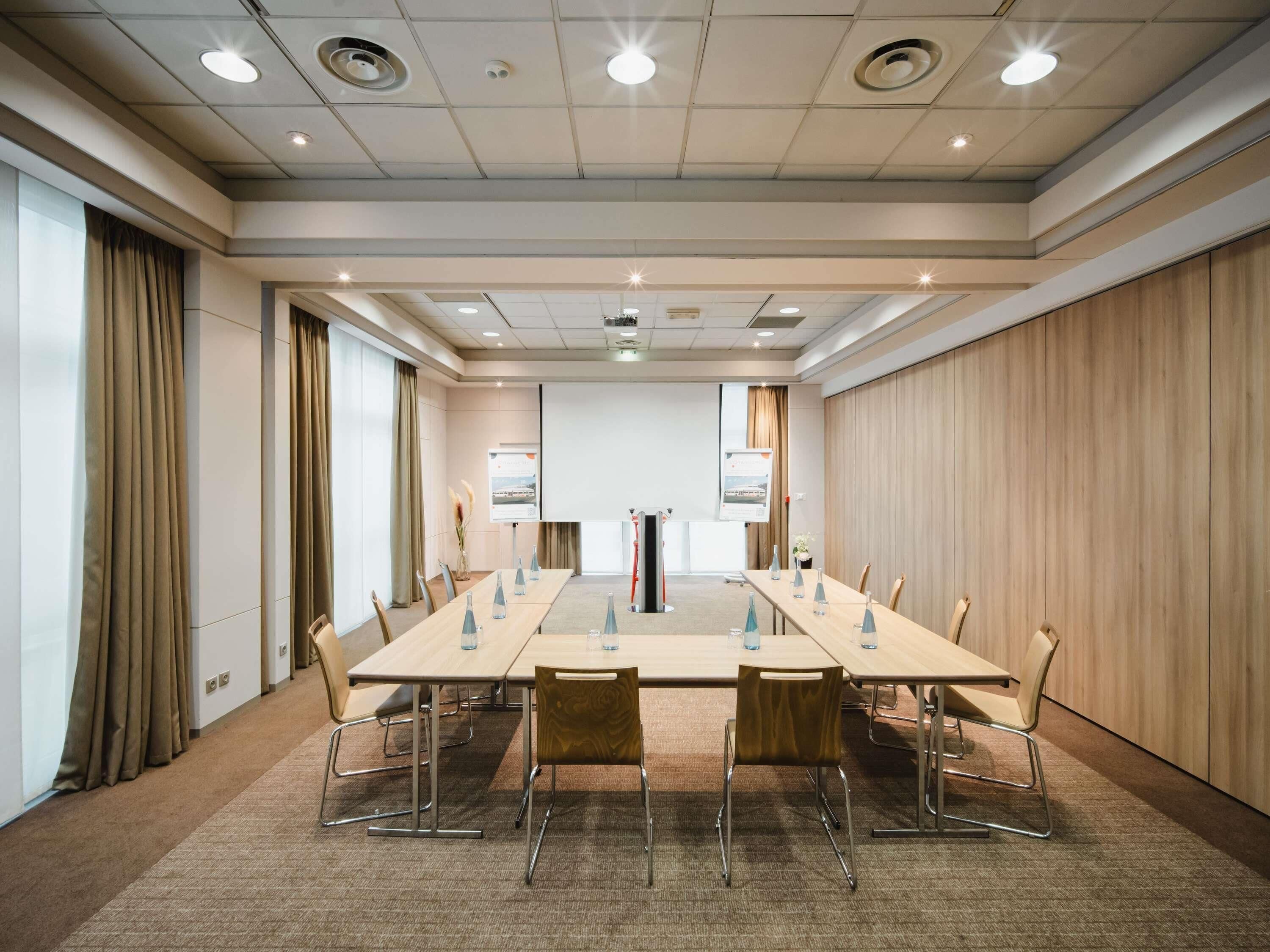 Uma sala de conferências com uma mesa comprida, cadeiras e uma tela de projeção.
