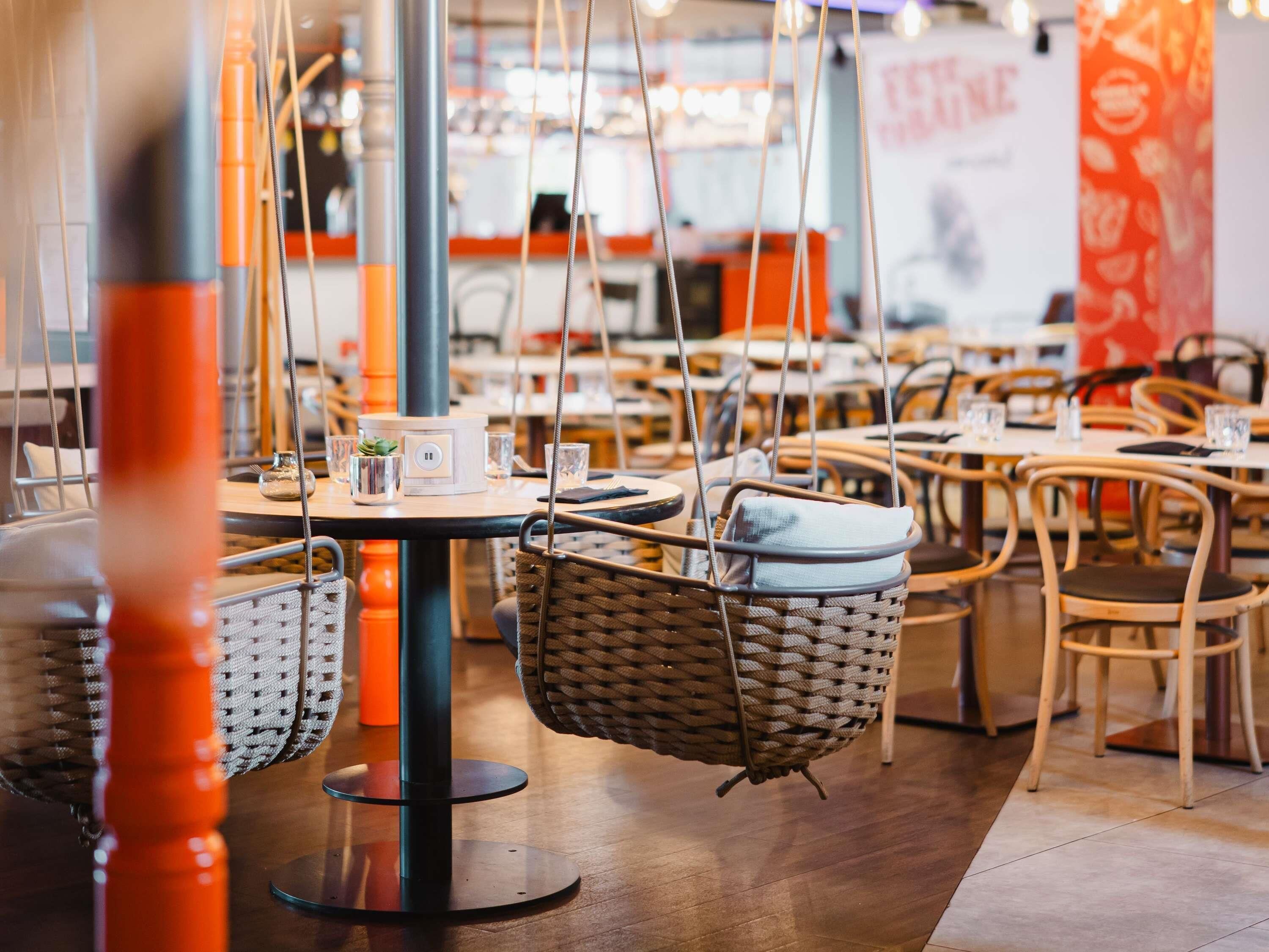 A modern restaurant with hanging wicker chairs, round tables, and a clean, organized layout.