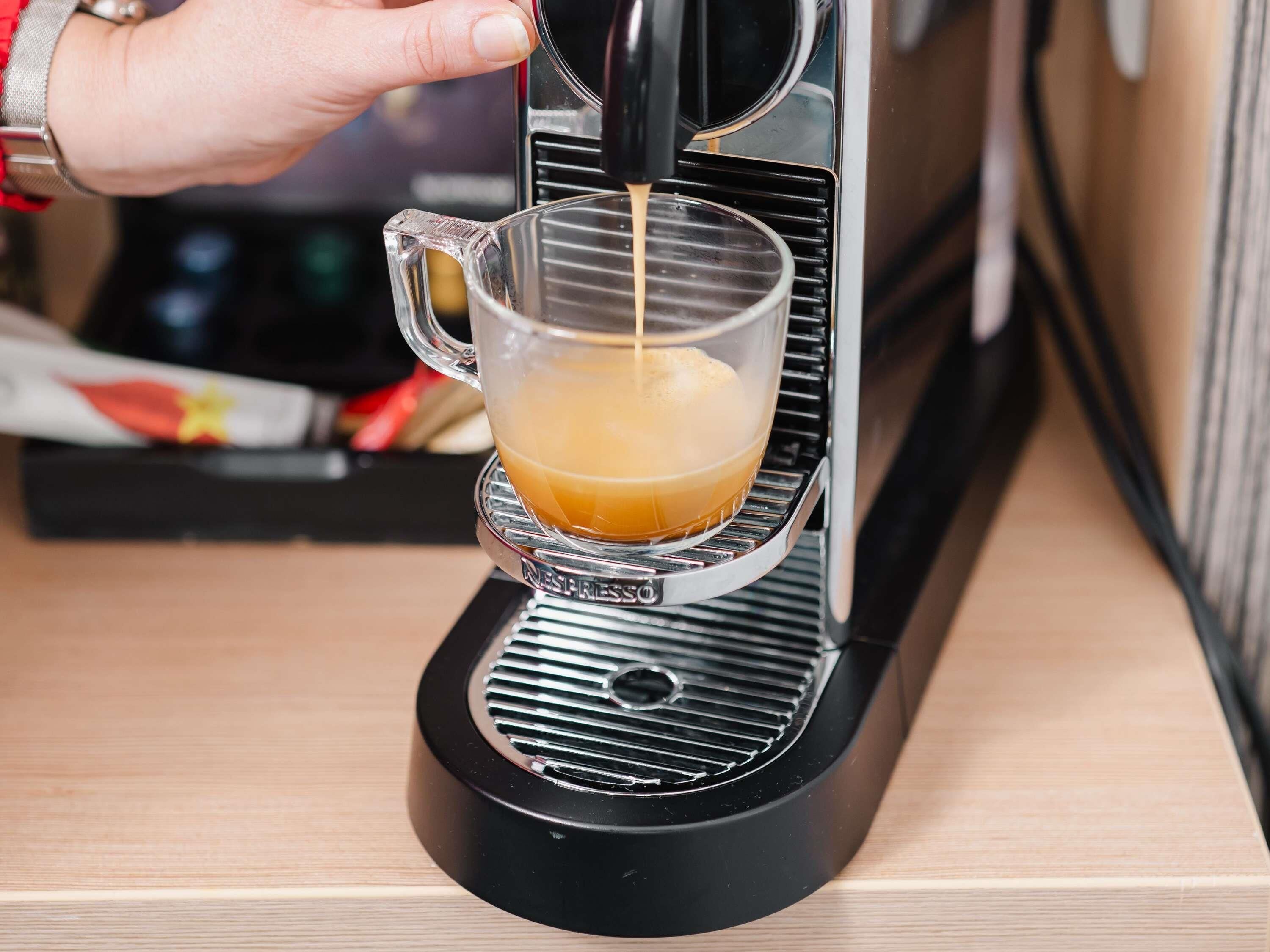 A person pouring coffee into a clear glass cup from a Nespresso machine.
