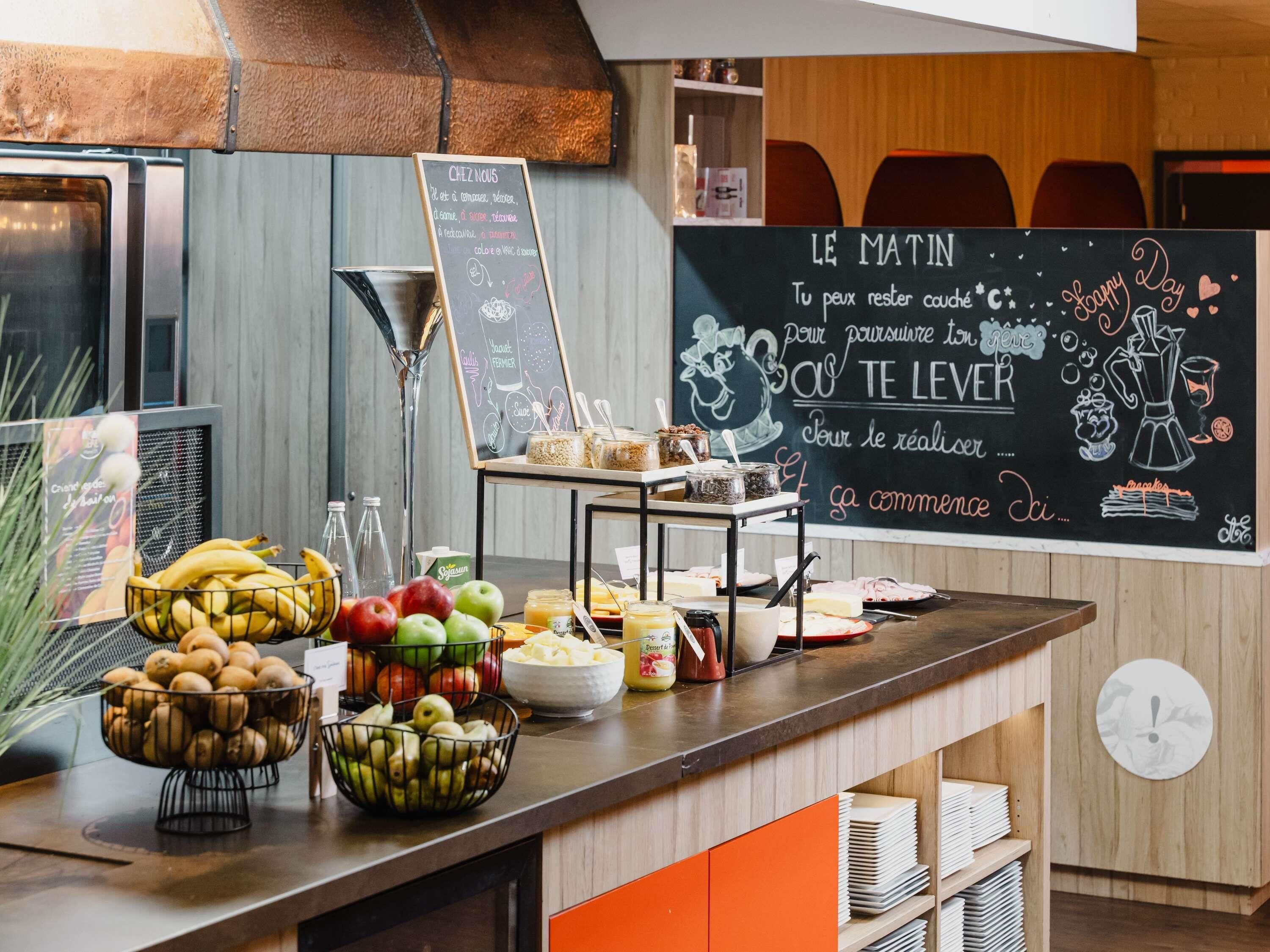 Een ontbijtbuffet met verschillende soorten fruit, een koffieapparaat en een krijtbordmenu.