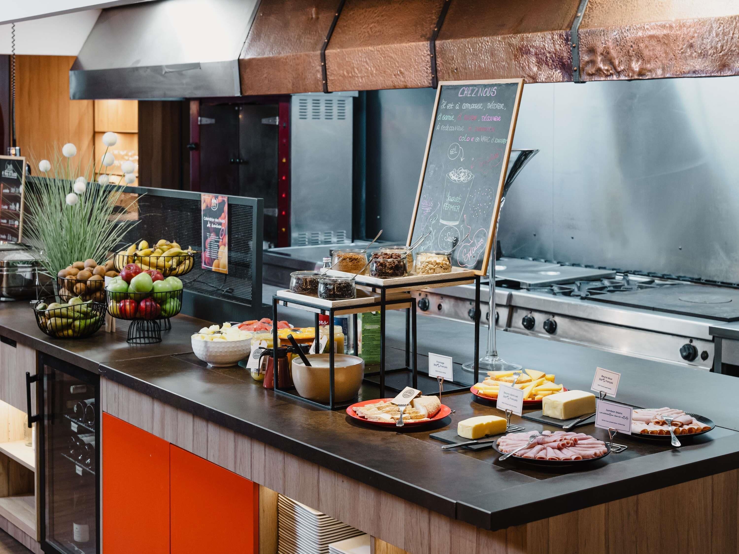 Zona de buffet con diversas opciones de comida, un menú en una pizarra y una cocina al fondo.