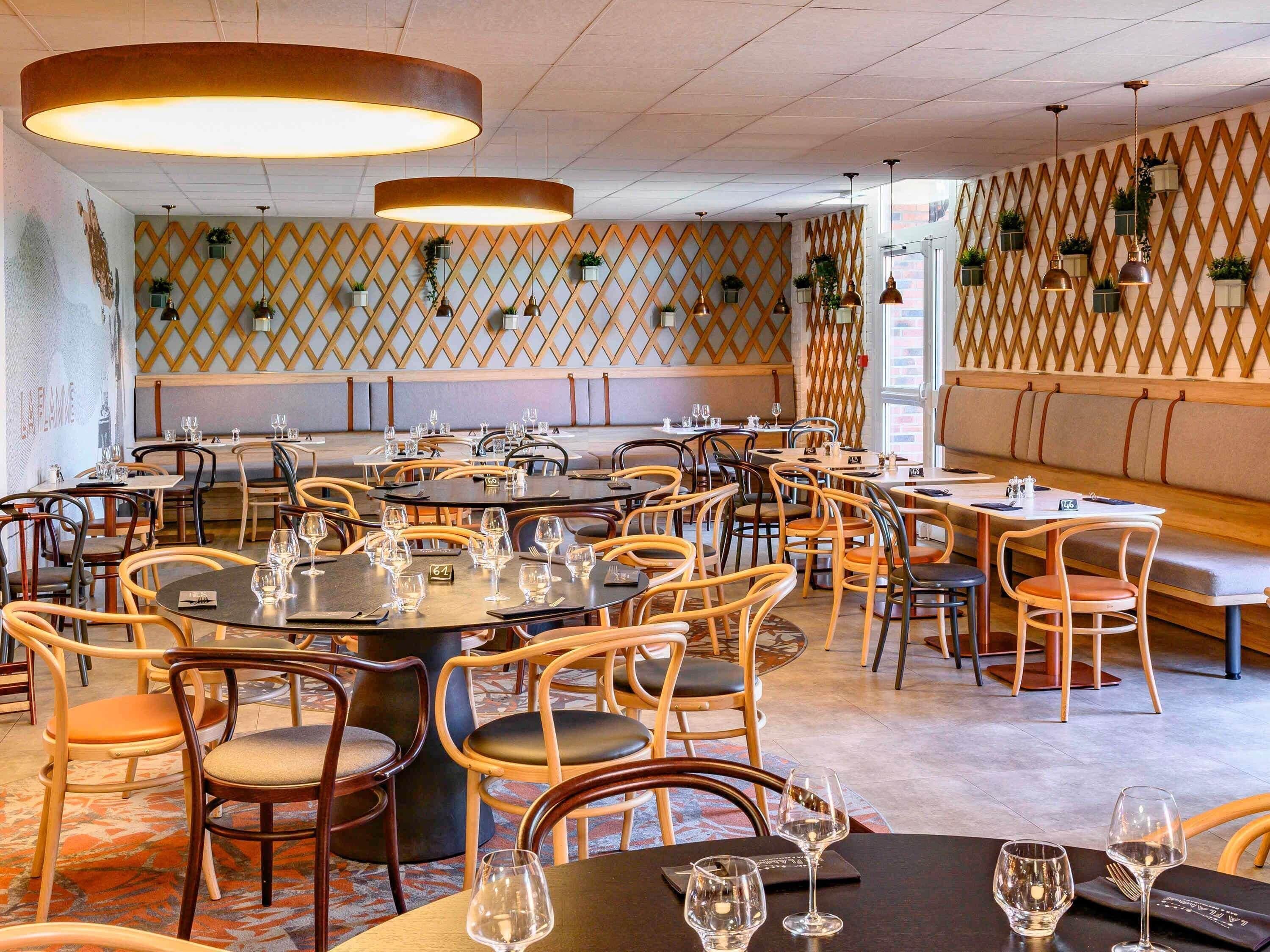 L’intérieur d’un restaurant avec des tables rondes, des chaises et des lampes suspendues.