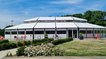 A modern building with a flat roof and large windows, surrounded by a landscaped garden with white flowers and green shrubs.