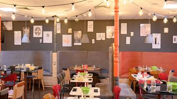 En restaurang med avskilda bås och bord, ljusslingor och inramade konstverk på väggarna.