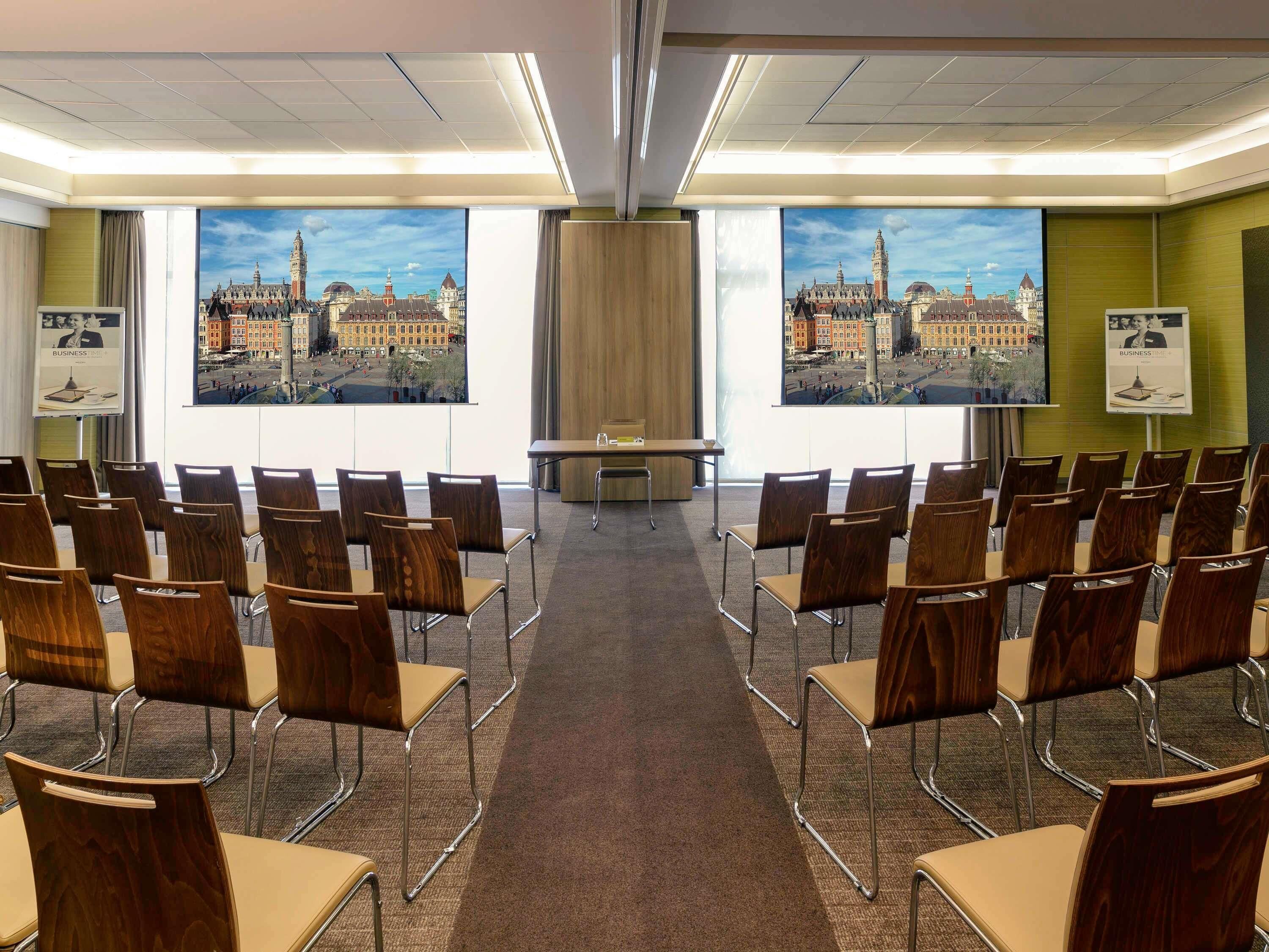 Een vergaderzaal met rijen stoelen gericht op een groot scherm waarop een stadsgezicht wordt weergegeven.