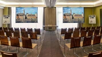 Een vergaderzaal met rijen stoelen gericht op een groot scherm waarop een stadsgezicht wordt weergegeven.
