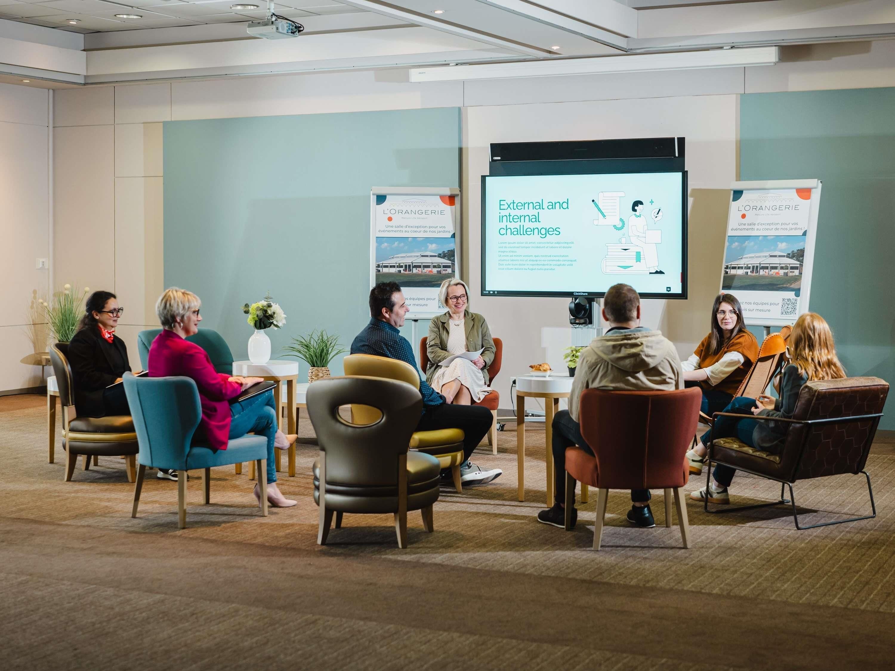 A group of people seated in a conference room with a presentation screen in the background.