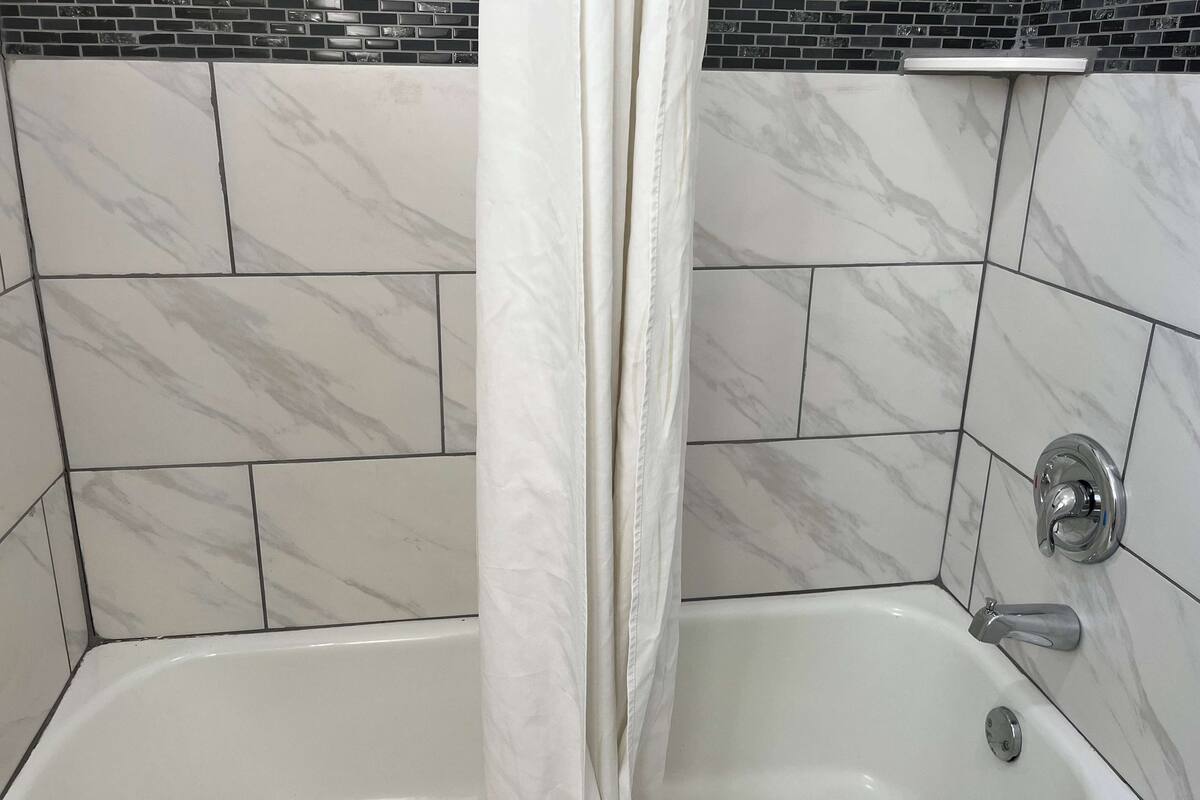 Ein Badezimmer mit einer weißen Badewanne, einem chromfarbenen Wasserhahn und einer Duschvorhang.