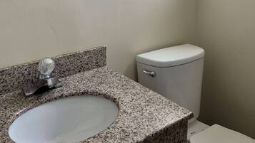 A bathroom with a granite countertop sink and a white toilet.