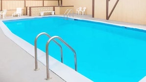 Ein Pool mit Metallleitern, weißen Stühlen und einer beigen Wand.