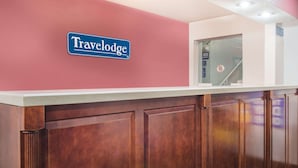 Ein Empfangsbereich mit einem 'Travelodge'-Schild, Holzsärchen und einer Glastür zum Treppenhaus.
