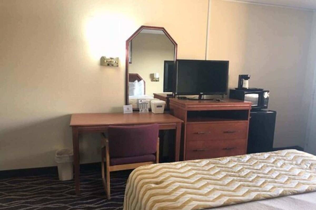 Ein Hotelzimmer mit einem Bett, einem Schreibtisch mit Stuhl, einem Fernseher, einer Kaffeemaschine und einem Mülleimer.