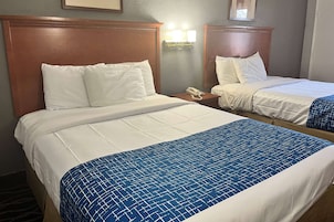 A hotel room with two beds, each with white bedding and a wooden headboard. There is a bedside table with a telephone on it.