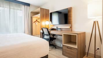 A hotel room with a bed, desk, chair, TV, lamp, and wardrobe.