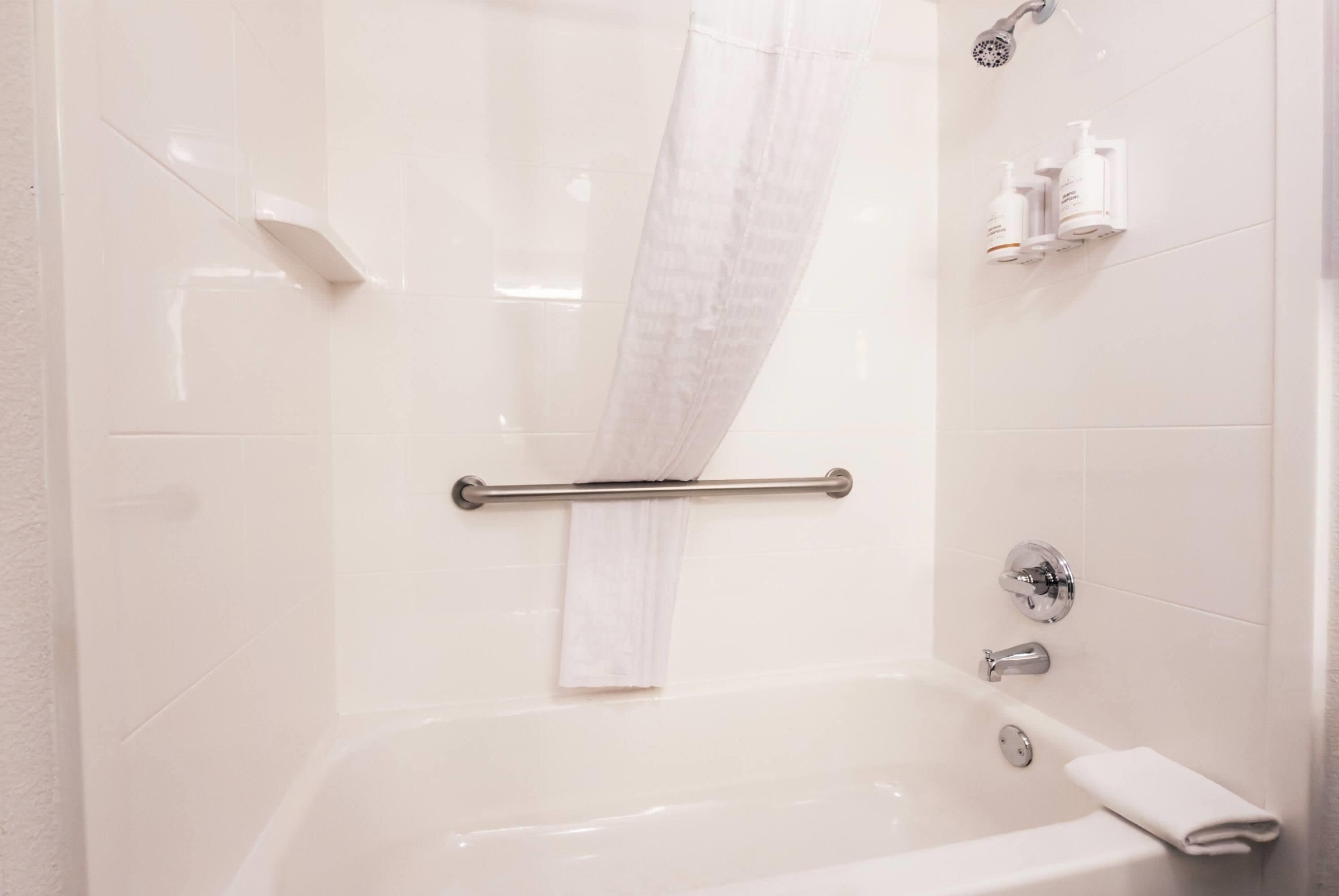 Une salle de bain avec une baignoire, un rideau de douche, un porte-serviettes et des articles de toilette rangés sur une étagère.
