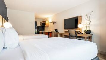 Habitación de hotel con cama, escritorio, silla, televisor y zona de cocina.