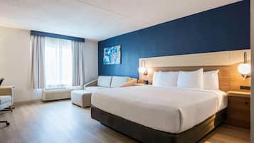 Habitación de hotel con una cama grande, un escritorio, una silla, un ventanal con cortinas y un cuadro en la pared.