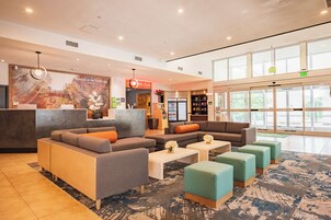 A hotel lobby with seating areas, a reception desk, and a large window providing natural light.