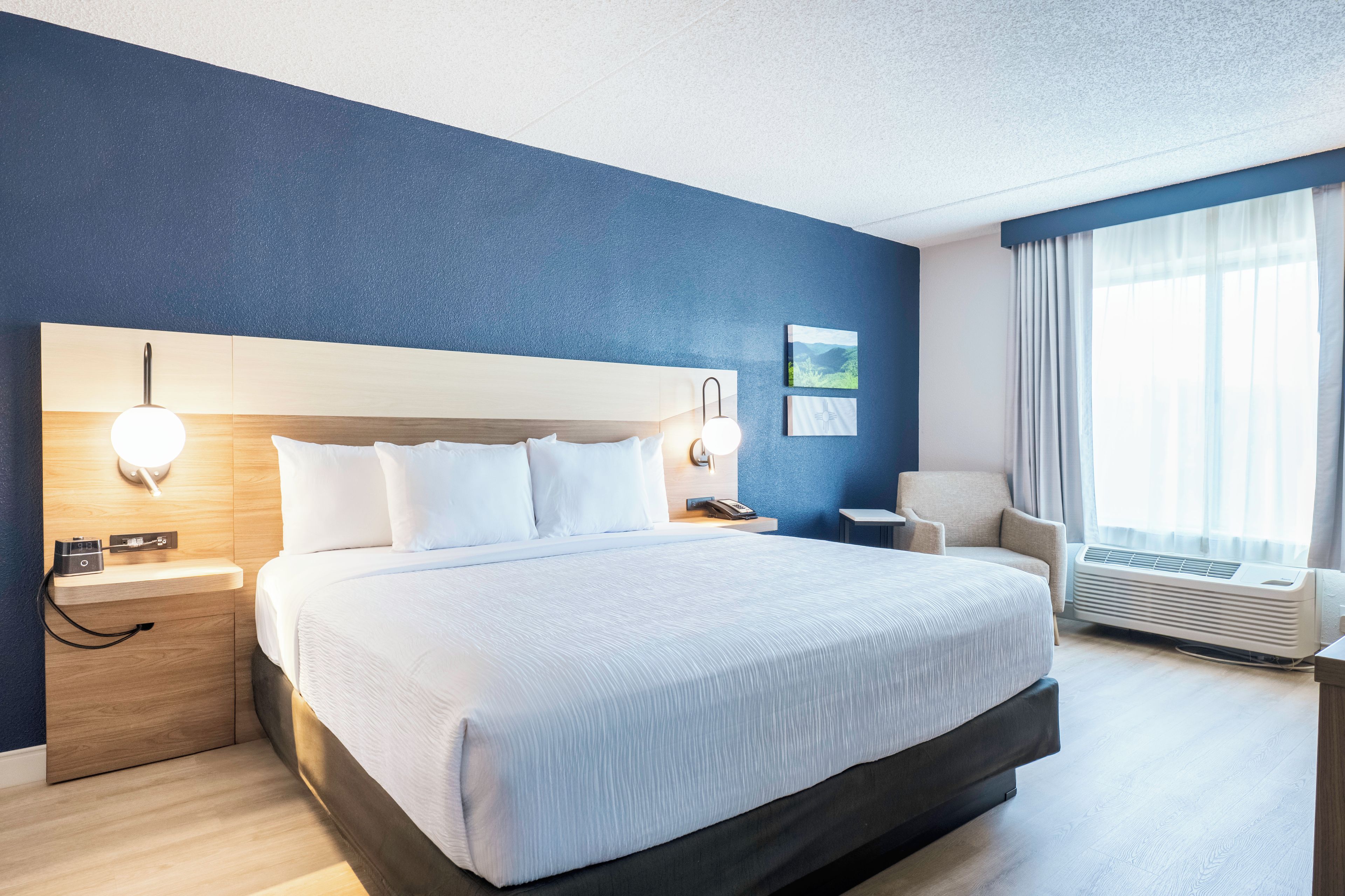 A hotel room with a large bed, bedside tables, a chair, a desk, and a window with curtains.
