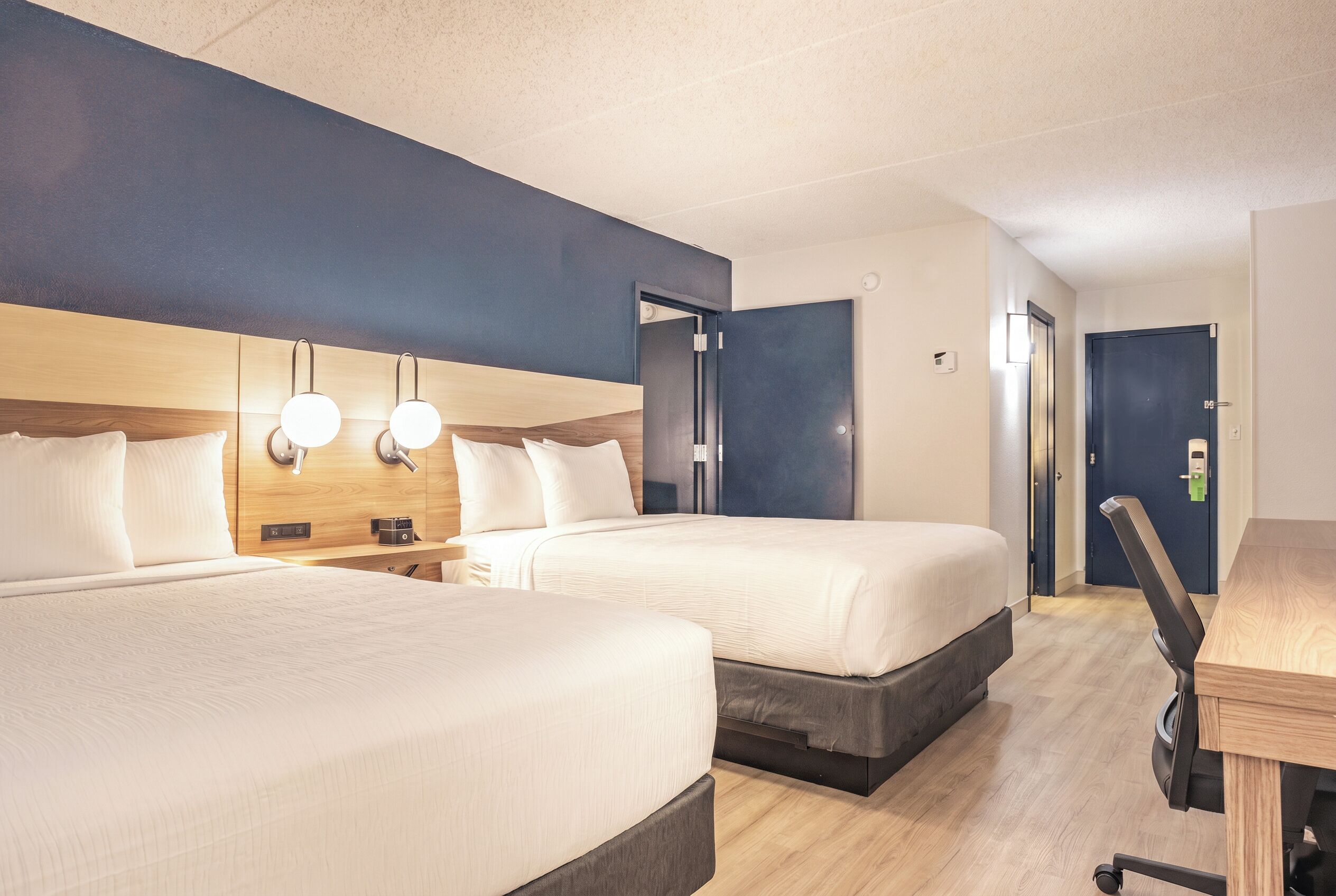 Een hotelkamer met twee bedden, een bureau en een deur.