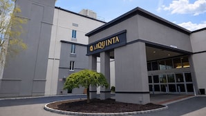 Un edificio moderno con un letrero que dice 'LAQUINTA' y un área ajardinada con un pequeño árbol.