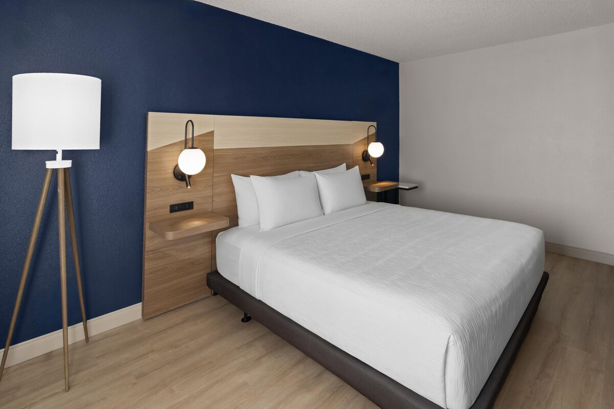 A modern bedroom with a wooden headboard, a large bed, two bedside lamps, and a floor lamp.