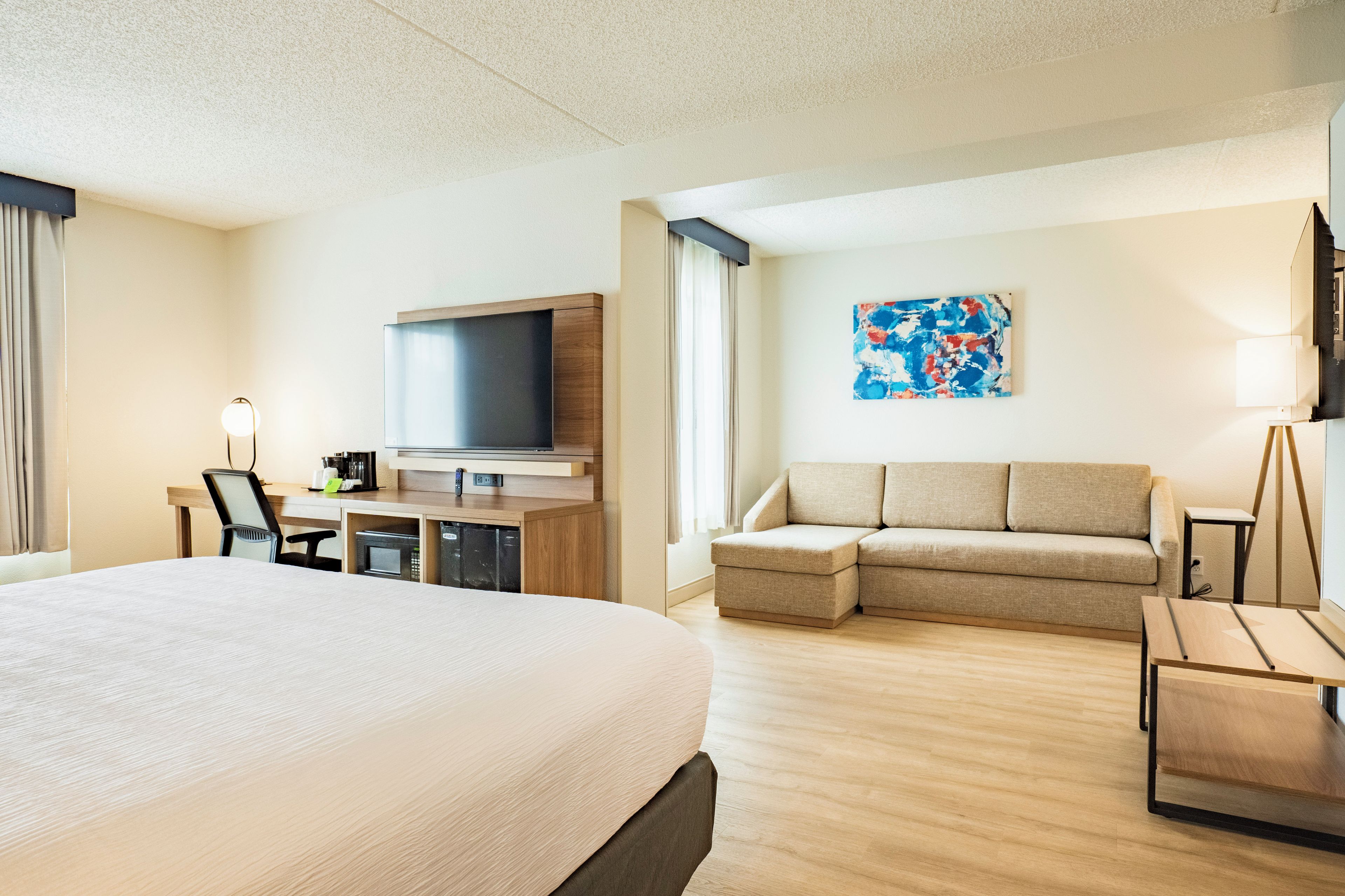 Una habitación de hotel con una cama grande, un televisor de pantalla plana, un sofá, un escritorio con lámpara y un cuadro en la pared.
