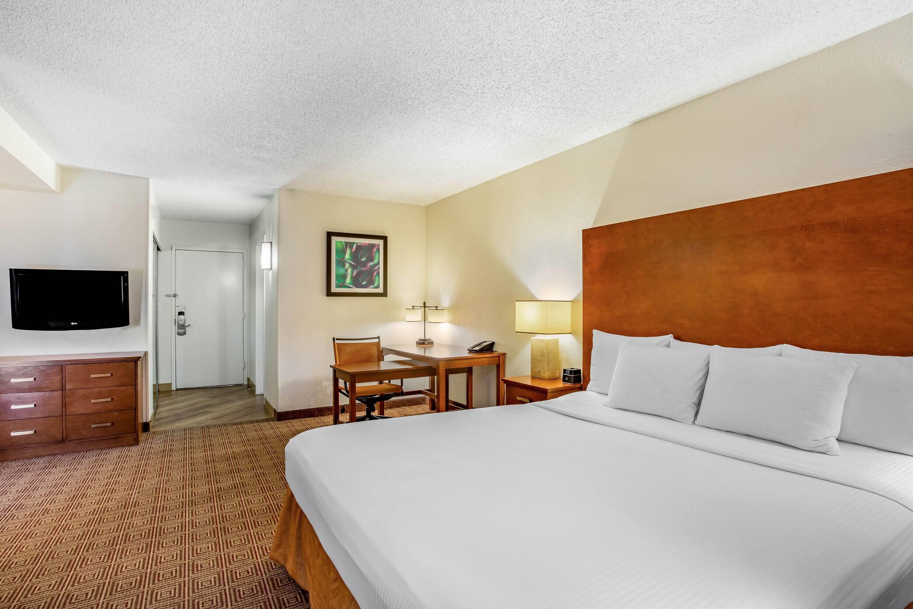 Ein Hotelzimmer mit Bett, Schreibtisch, Sessel, Fernseher und einer Tür.
