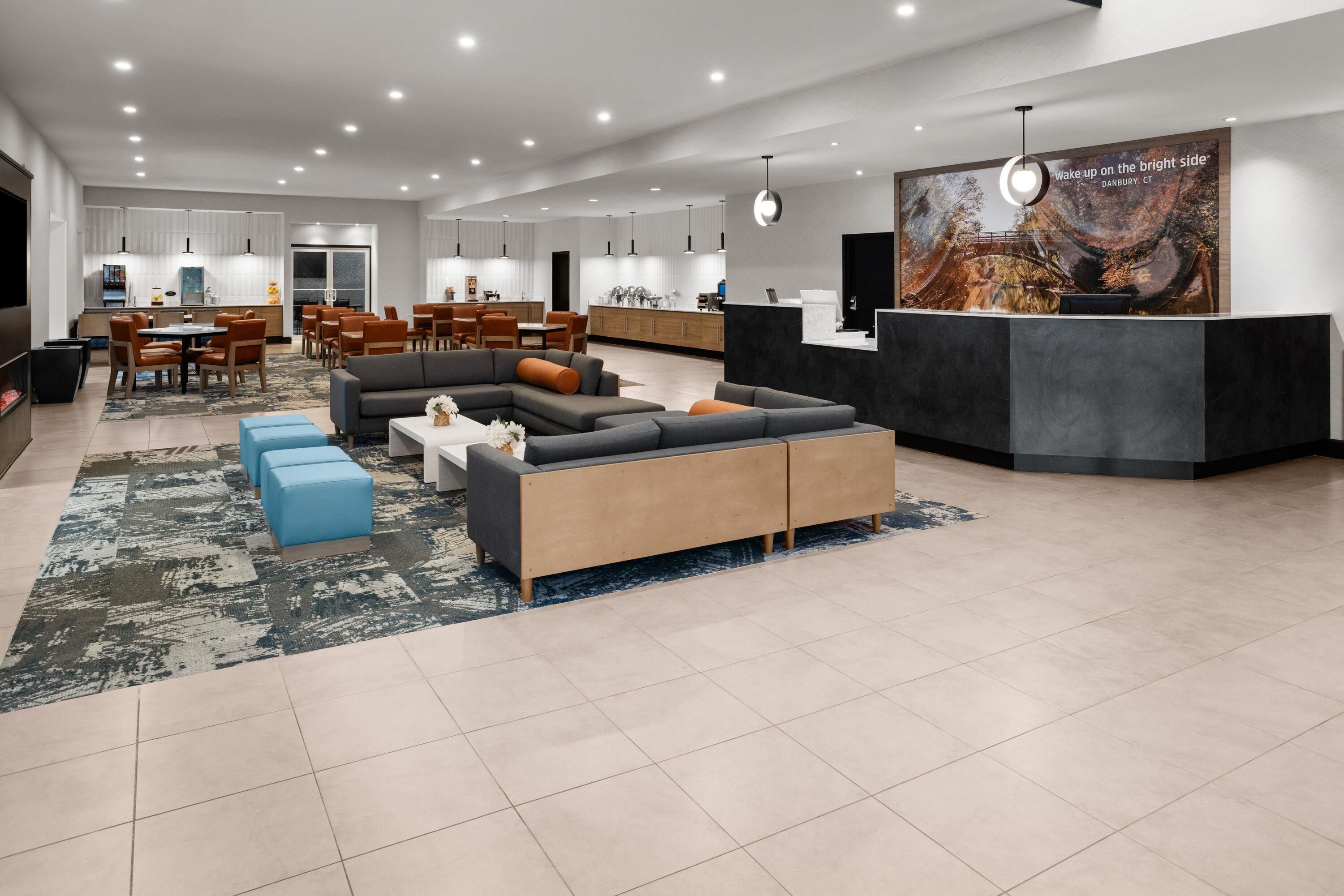 A modern hotel lobby with a seating area, a reception desk, and a dining area.