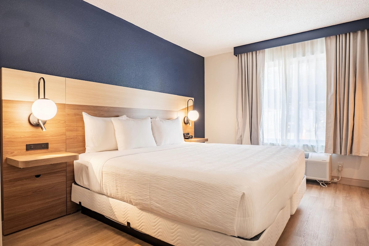 Une chambre d’hôtel avec un grand lit, une tête de lit en bois, des lampes de chevet, une table de chevet et une fenêtre avec des rideaux.