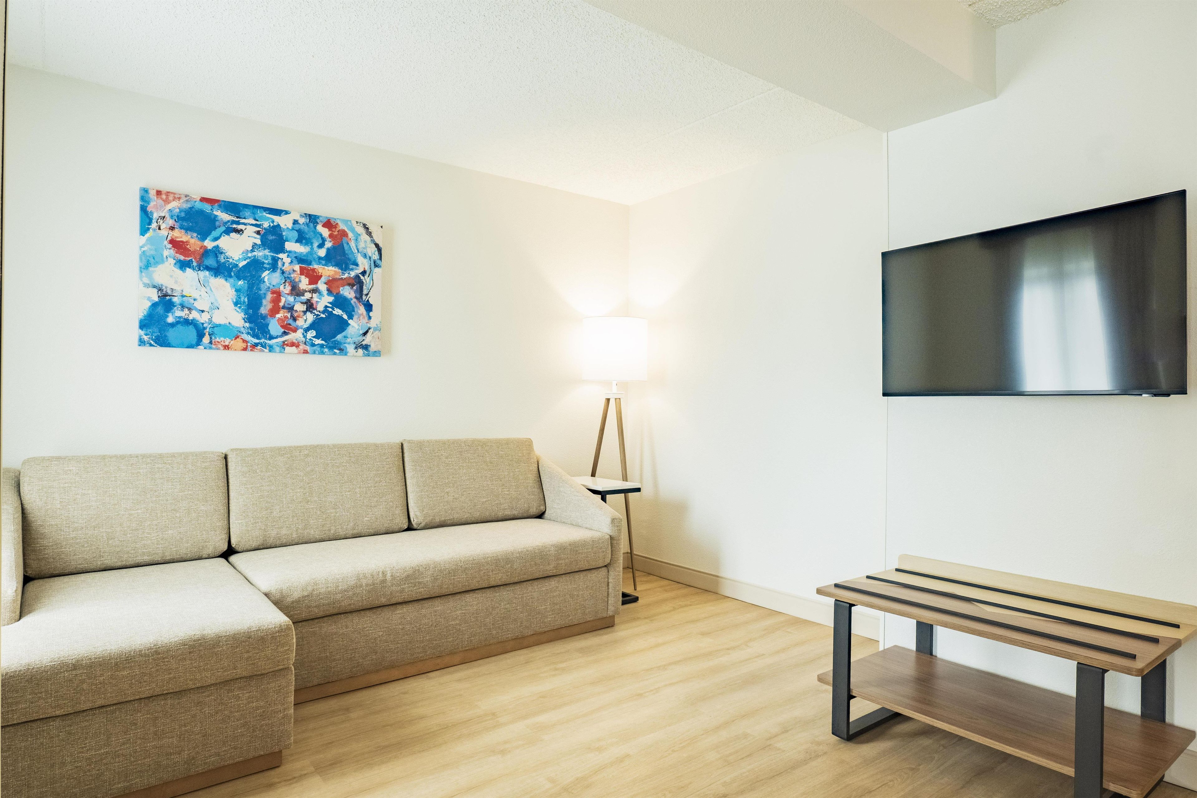 Una sala de estar moderna con un sofá color beige, un banco de madera, un televisor de pantalla plana y una lámpara de pie.