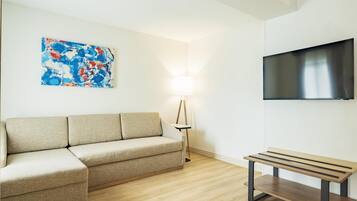 Una sala de estar moderna con un sofá color beige, un banco de madera, un televisor de pantalla plana y una lámpara de pie.