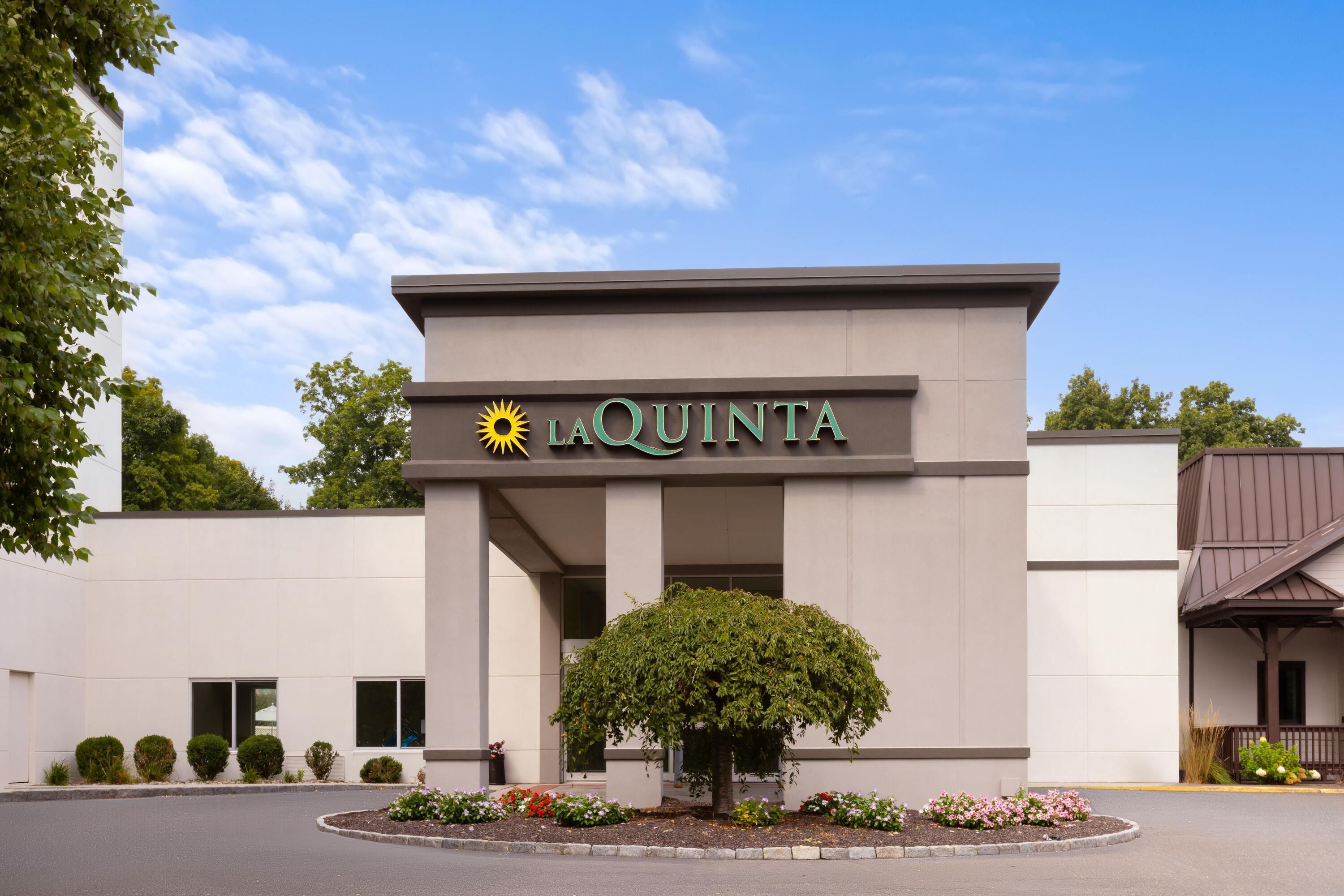 A La Quinta hotel entrance with a clear sky, a large sun emblem, and a well-maintained garden.