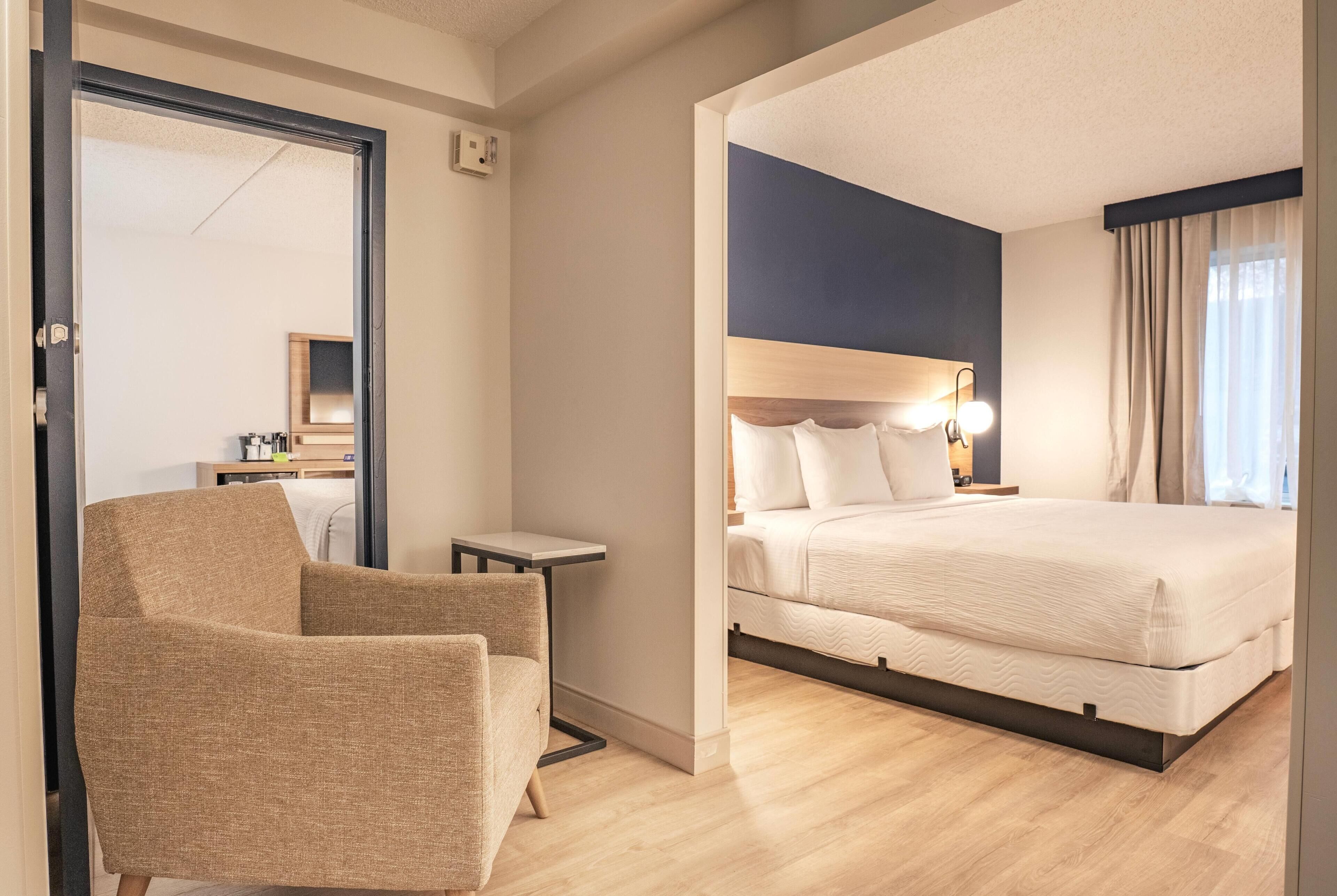 Ein Hotelzimmer mit Bett, Stuhl, kleinem Tisch und Spiegel.