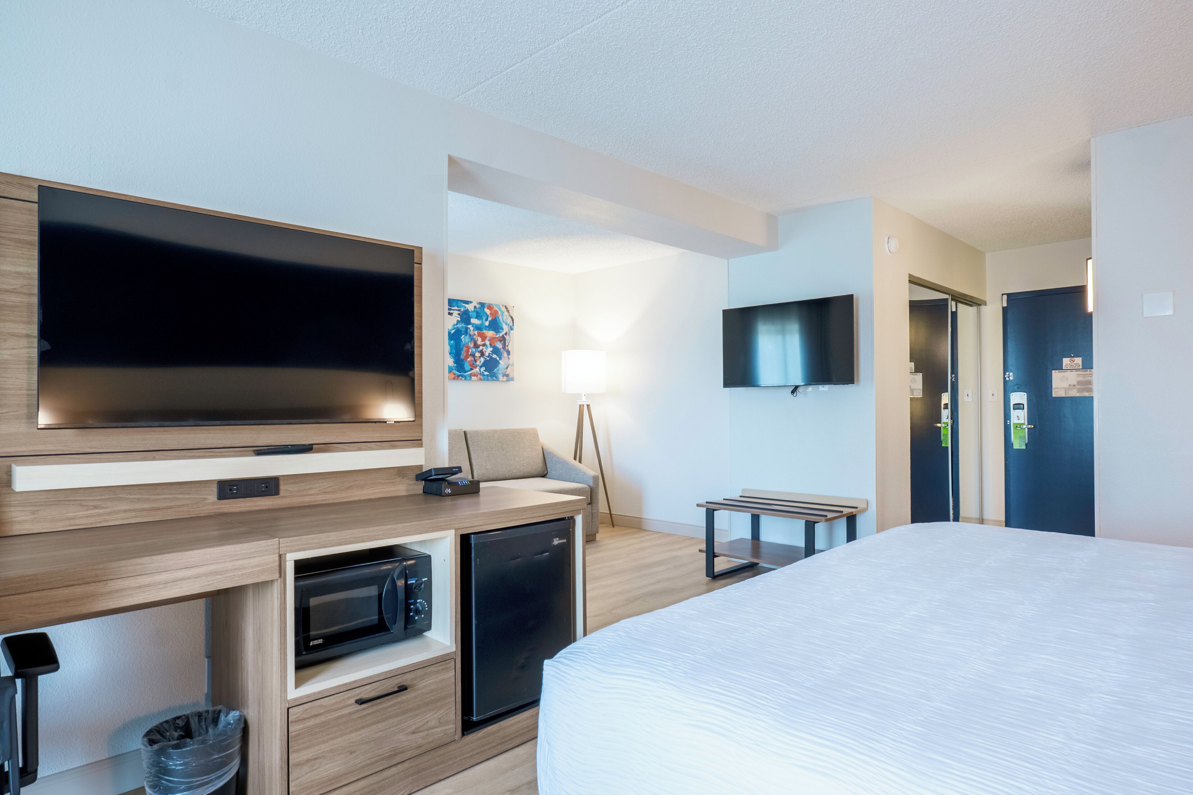 Une chambre d’hôtel moderne équipée d’un lit, d’une télévision, d’un four à micro-ondes et d’un bureau avec une chaise.