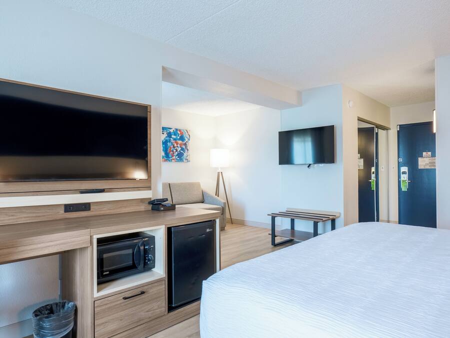 Une chambre d’hôtel moderne équipée d’un lit, d’une télévision, d’un four à micro-ondes et d’un bureau avec une chaise.