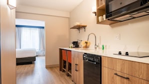 Habitación de hotel pequeña con kitchenette, cama y vistas al exterior.