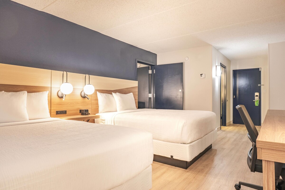 A hotel room with two beds, a desk, and a chair.