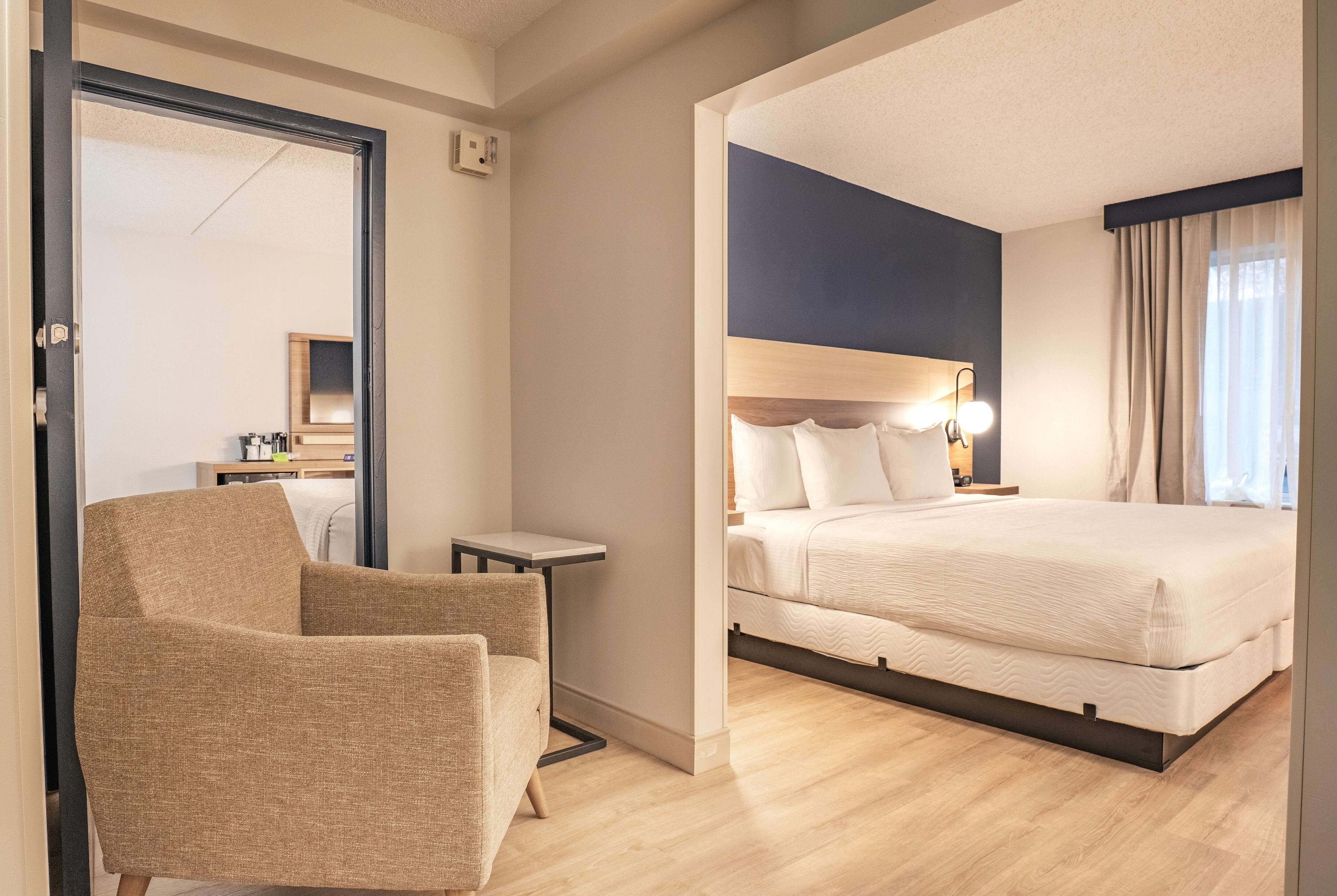 Una camera d'albergo con un letto, una sedia, un tavolino e uno specchio.