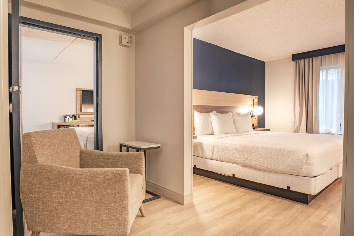 A hotel room with a bed, a chair, a small table, and a mirror.