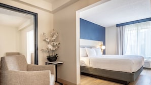 Habitación de hotel con cama, una silla, una mesita con una planta y un espejo.