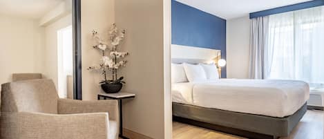 Habitación de hotel con cama, una silla, una mesita con una planta y un espejo.
