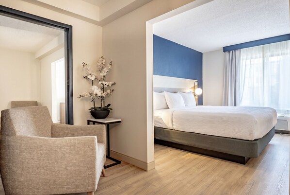 A hotel room with a bed, a chair, a small table with a plant, and a mirror. - La Quinta Inn & Suites by Wyndham Danbury (Danbury)
