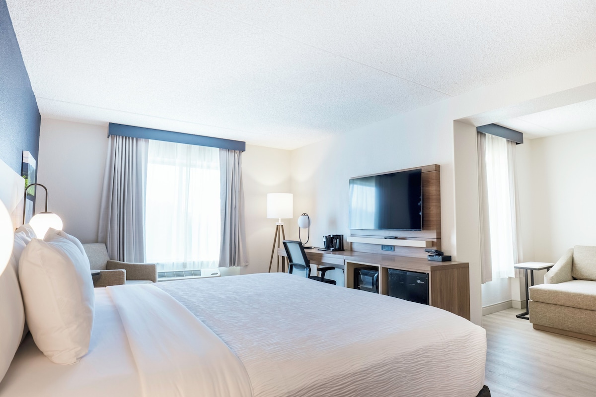 A hotel room with a large bed, a desk with a flat-screen TV, a chair, and a sofa.