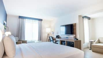 A hotel room with a large bed, a desk with a flat-screen TV, a chair, and a sofa.