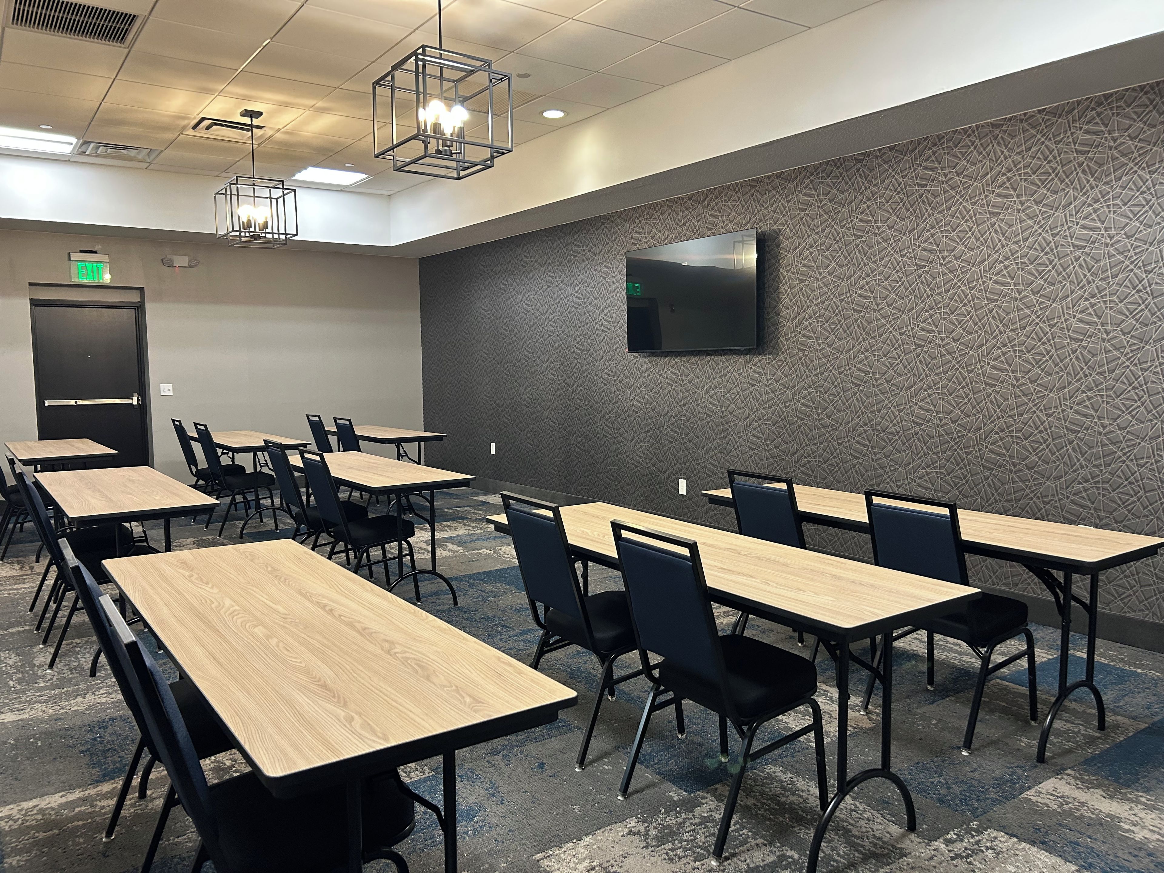 A conference room with multiple tables and chairs, a flat-screen TV mounted on the wall, and an exit sign.