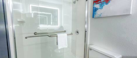 A modern bathroom with a glass shower enclosure, a white toilet, and a small shelf.