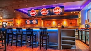 Zona de bar con varios letreros de VANS, mostrador de bar de madera y varios taburetes.