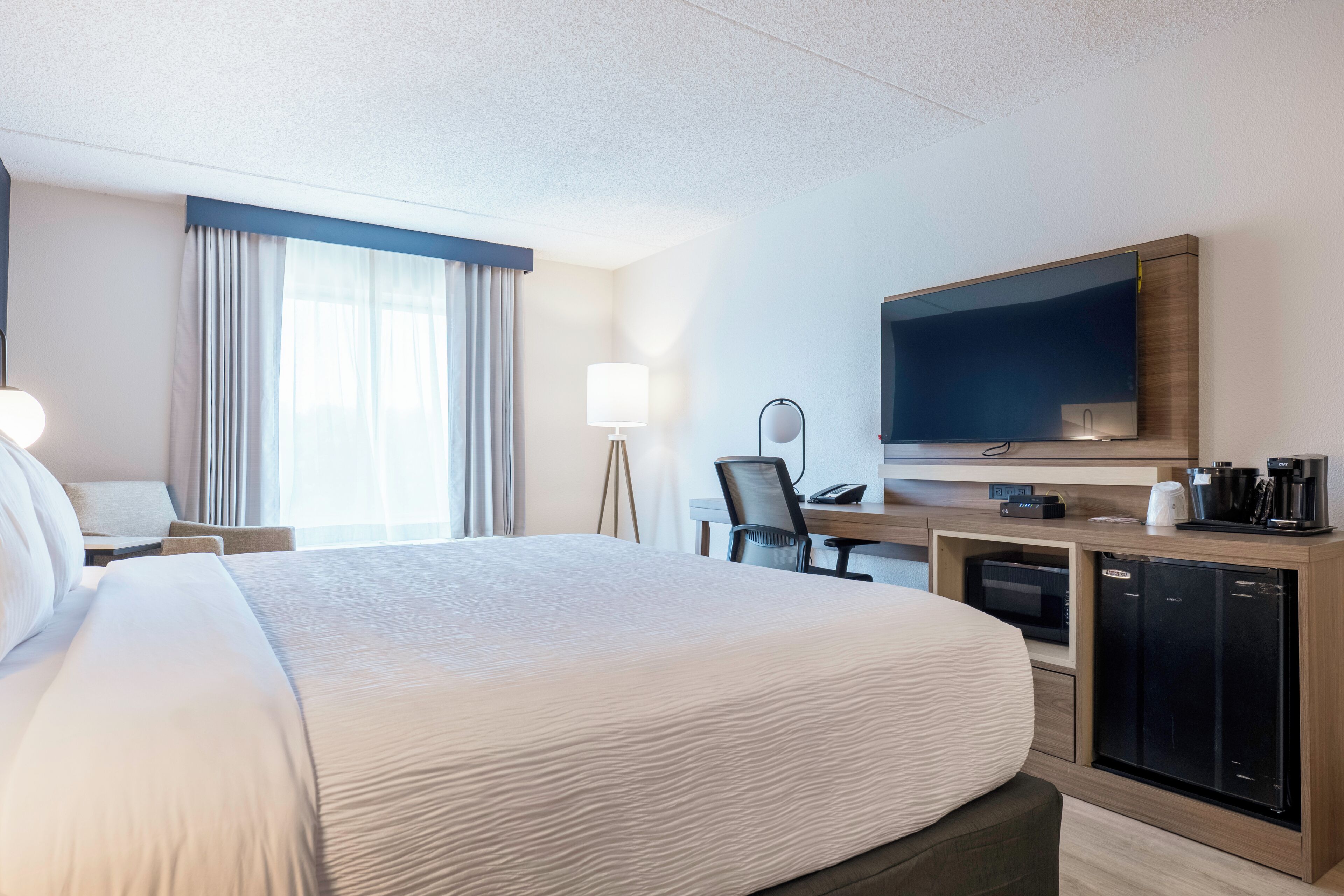 A hotel room with a large bed, a desk with a chair, a television, a coffee maker, and a microwave.