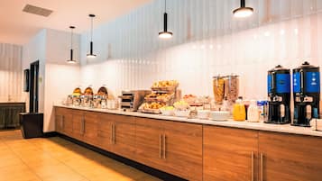 A breakfast buffet with various food items, coffee machines, and a modern kitchen design.